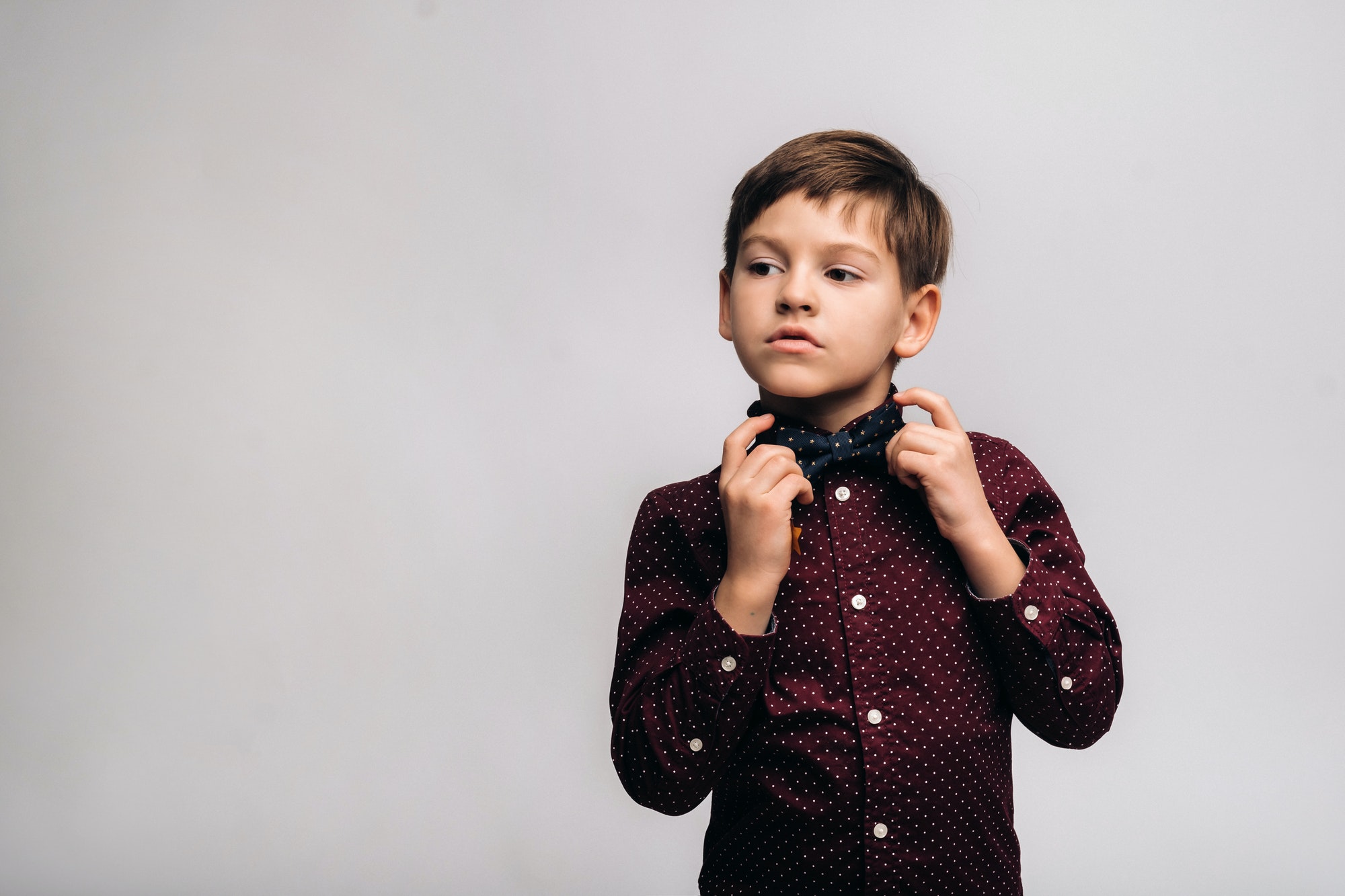 a beautiful boy in a shirt and bow tie stands on a gray background.jpg