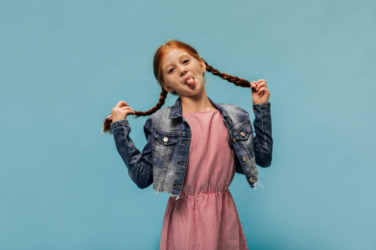 funny girl with ginger hair and freckles in striped red dress and fashionable cool jacket showing t.jpg